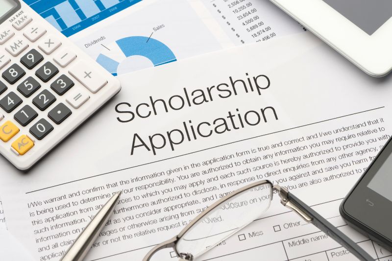 A close-up of a scholarship application form surrounded by a calculator, eyeglasses, pen, smartphone, tablet, and financial charts, representing the process of applying for educational financial aid.